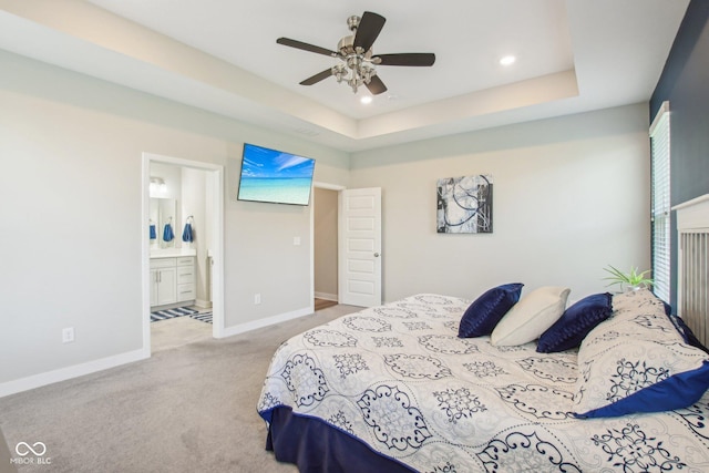 carpeted bedroom featuring recessed lighting, ensuite bath, baseboards, a raised ceiling, and a ceiling fan