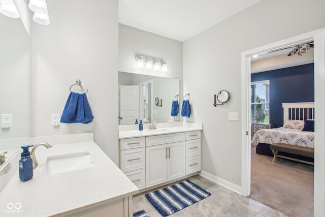 full bath with connected bathroom, two vanities, a sink, and baseboards