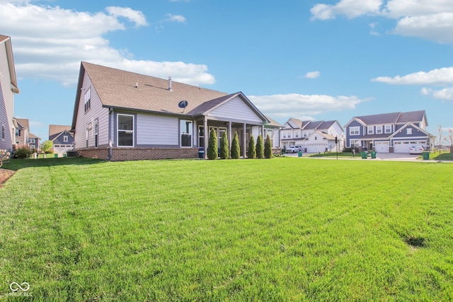 rear view of house featuring a residential view, a lawn, a sunroom, and roof with shingles