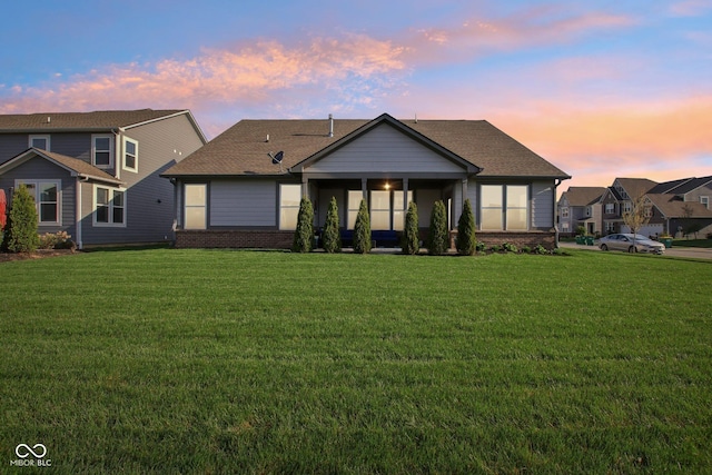 view of front of property with brick siding, a shingled roof, a front lawn, and a sunroom