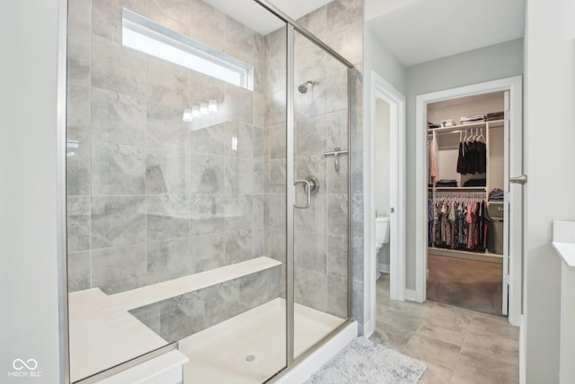 full bathroom featuring a spacious closet, a stall shower, and toilet
