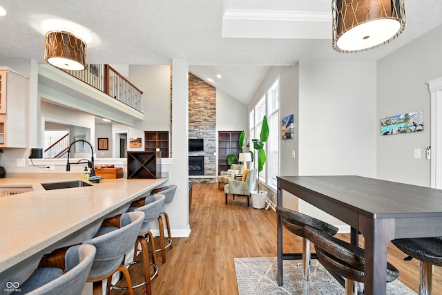 dining room with a stone fireplace, crown molding, stairway, light wood finished floors, and lofted ceiling