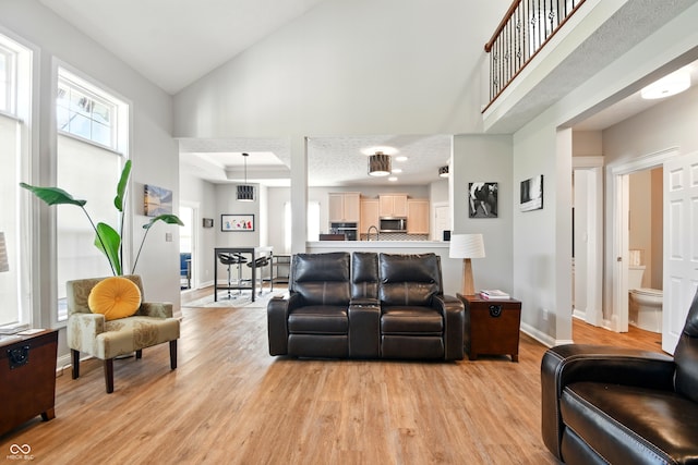 living room featuring baseboards, light wood finished floors, visible vents, and high vaulted ceiling