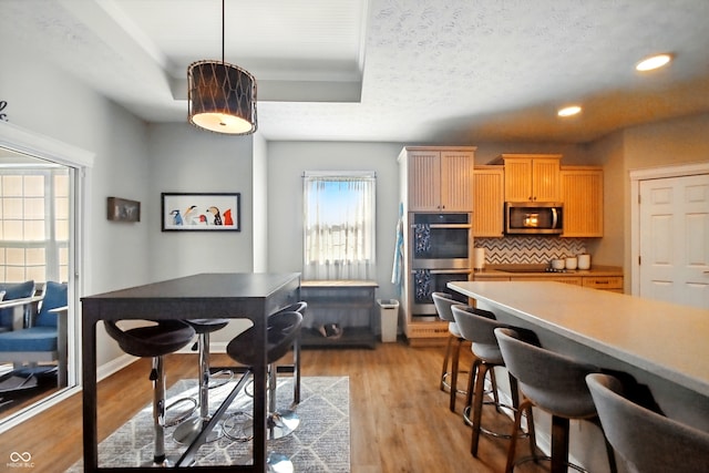 kitchen with appliances with stainless steel finishes, tasteful backsplash, light wood-style floors, a breakfast bar, and recessed lighting