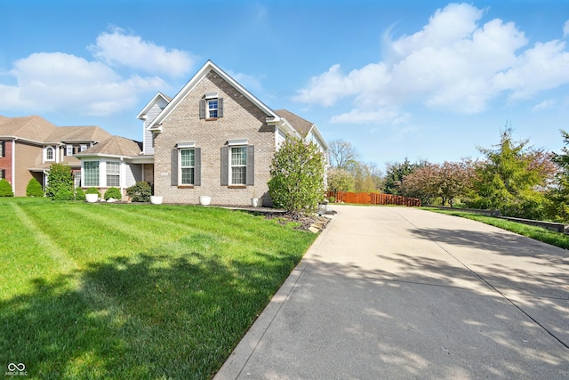 traditional-style home with fence, driveway, a front lawn, and brick siding