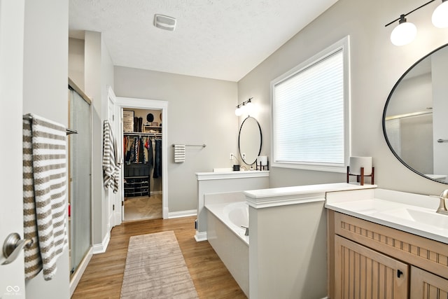 full bath with a garden tub, vanity, wood finished floors, a walk in closet, and a stall shower