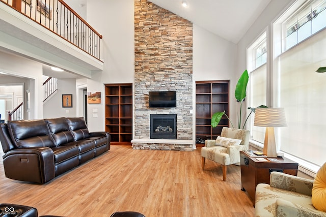living room featuring a stone fireplace, wood finished floors, high vaulted ceiling, and stairway