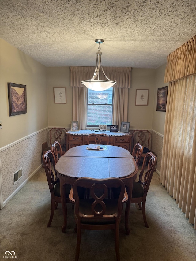 dining area featuring light carpet, a wainscoted wall, visible vents, and a textured ceiling
