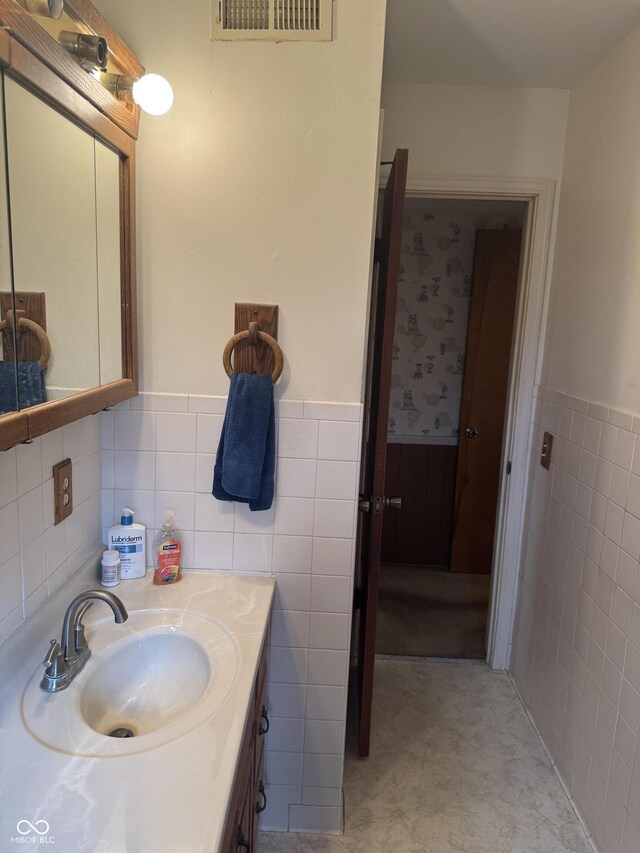 bathroom featuring tile walls, visible vents, vanity, and wainscoting