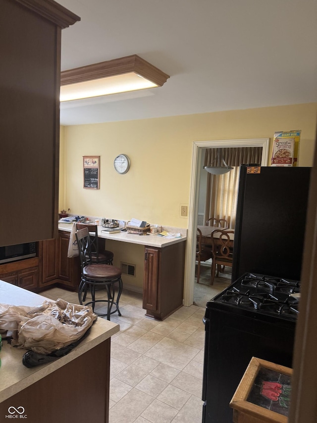kitchen featuring dark brown cabinets, built in desk, black appliances, light countertops, and visible vents