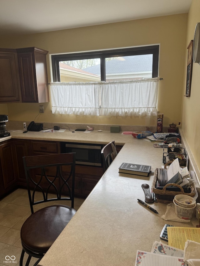 kitchen featuring stainless steel microwave, light tile patterned flooring, dark brown cabinets, and light countertops
