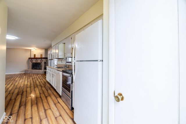 8899 E Southshore Dr, Unionville, IN 47468 - kitchen featuring electric stove, a sink, freestanding refrigerator, light wood-style floors, and a brick fireplace