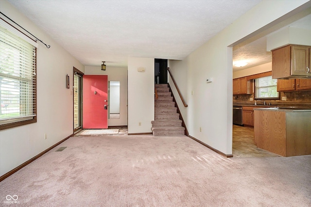 unfurnished living room featuring stairway, light carpet, a sink, and baseboards