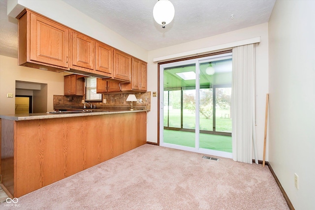 kitchen featuring a peninsula, brown cabinetry, tasteful backsplash, visible vents, and light carpet