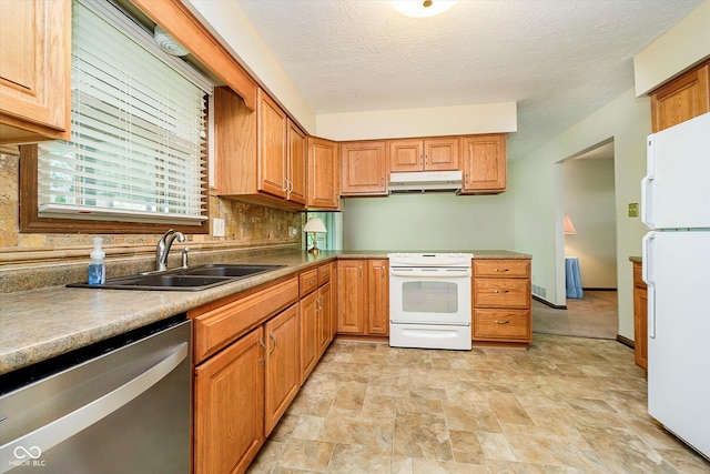 kitchen with a sink, white appliances, a textured ceiling, under cabinet range hood, and stone finish flooring