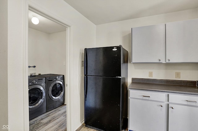 kitchen featuring washer and clothes dryer, dark countertops, freestanding refrigerator, light wood-style floors, and white cabinetry