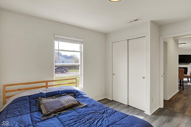 bedroom with baseboards, wood finished floors, visible vents, and a closet