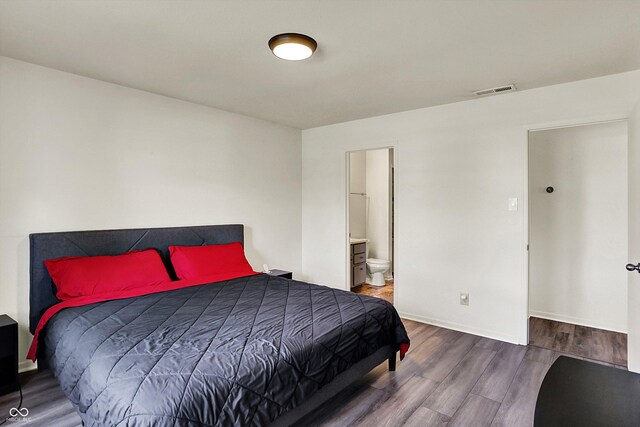 bedroom featuring visible vents, baseboards, wood finished floors, and connected bathroom