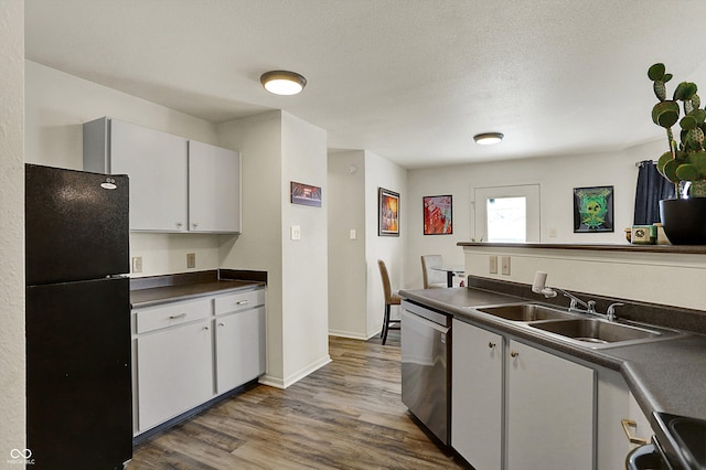 kitchen featuring dark wood finished floors, stainless steel appliances, dark countertops, a sink, and baseboards