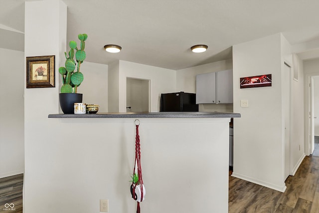 kitchen with a peninsula, baseboards, dark wood-type flooring, and black fridge