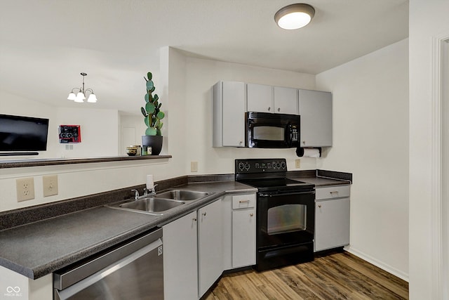 kitchen with a sink, dark countertops, a notable chandelier, wood finished floors, and black appliances
