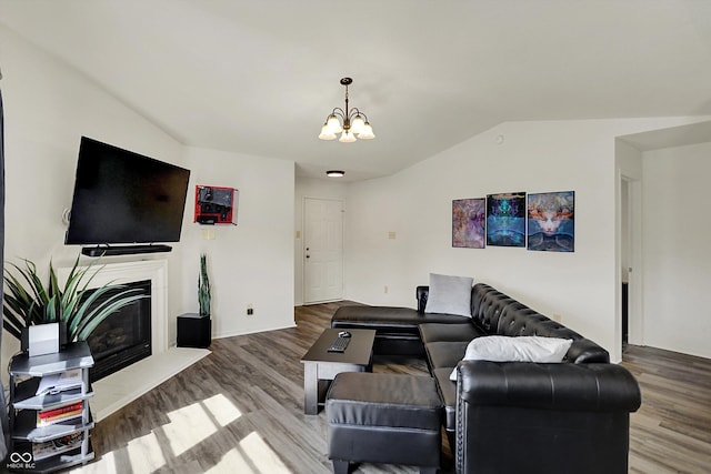 living room with lofted ceiling, a notable chandelier, a glass covered fireplace, and wood finished floors