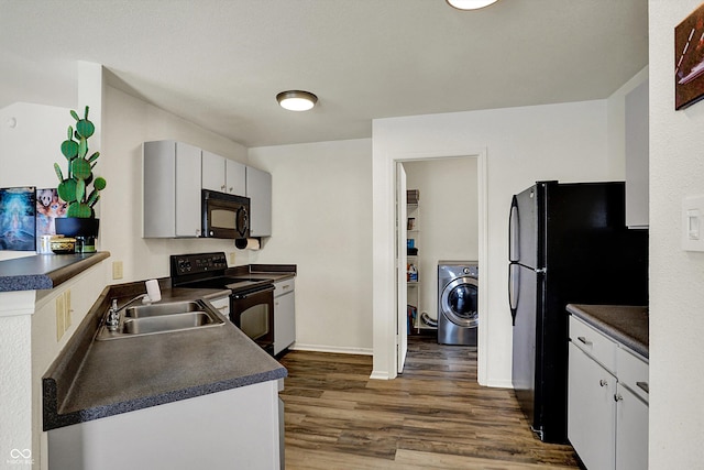 kitchen featuring dark countertops, a sink, black appliances, washer / dryer, and dark wood-style floors