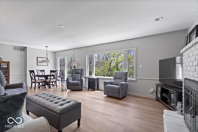 living area with visible vents, baseboards, a glass covered fireplace, and wood finished floors