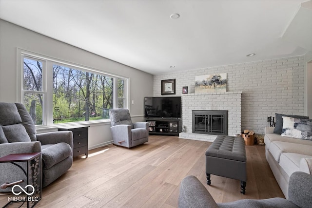 living room featuring baseboards, a brick fireplace, and light wood-style flooring