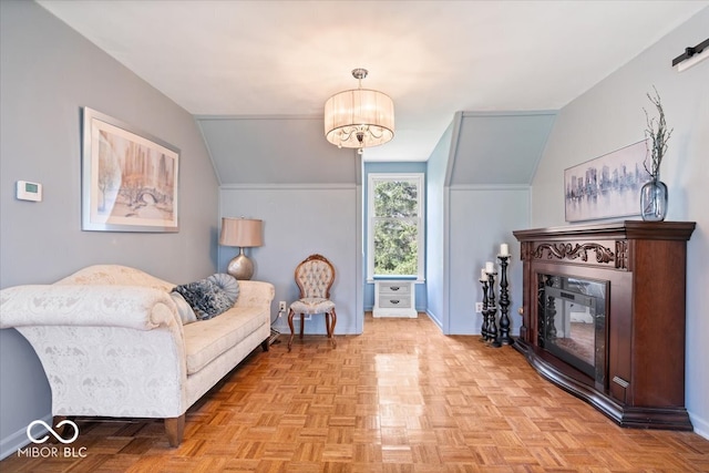 sitting room with baseboards, a glass covered fireplace, lofted ceiling, and a notable chandelier
