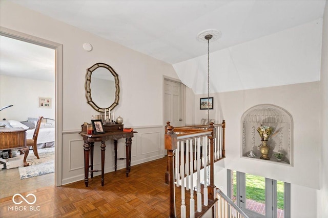 hall with a decorative wall, an upstairs landing, lofted ceiling, and a wainscoted wall