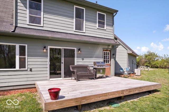 rear view of property with a lawn, a deck, and roof with shingles