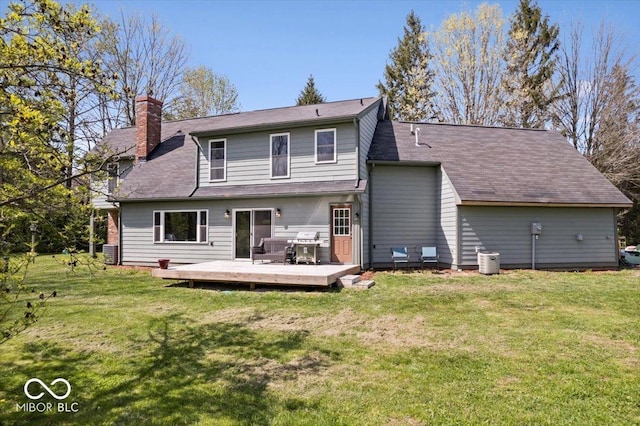 rear view of house featuring roof with shingles, a wooden deck, a yard, and a chimney