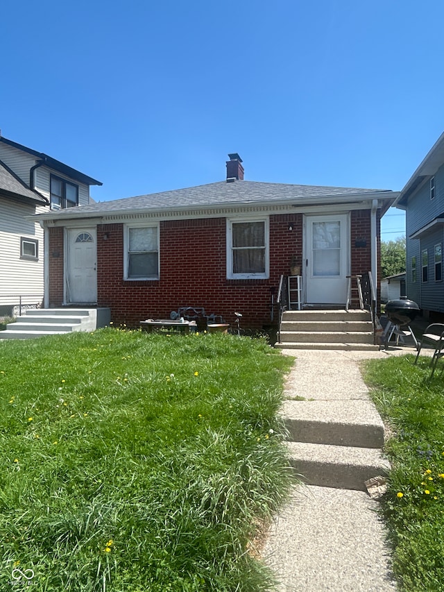 single story home featuring brick siding, a chimney, roof with shingles, and a front lawn