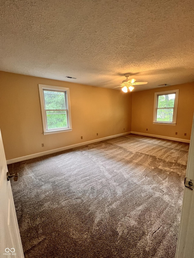 carpeted empty room featuring a textured ceiling, ceiling fan, and plenty of natural light