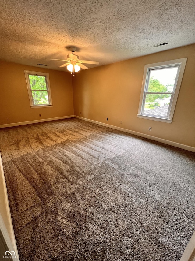 carpeted empty room featuring a textured ceiling, baseboards, a ceiling fan, and visible vents
