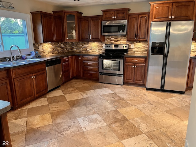 kitchen with a sink, stone tile floors, backsplash, and appliances with stainless steel finishes