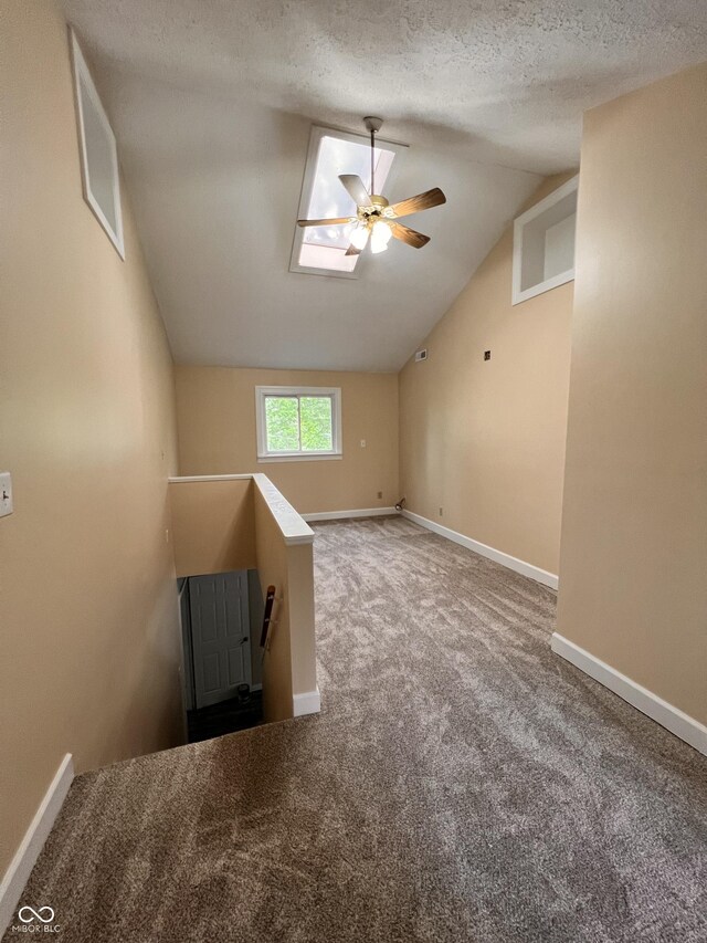 bonus room with a ceiling fan, vaulted ceiling with skylight, carpet floors, a textured ceiling, and baseboards