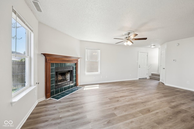unfurnished living room with a tiled fireplace, ceiling fan, stairway, and a textured ceiling