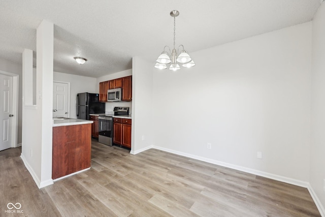 kitchen with appliances with stainless steel finishes, an inviting chandelier, light wood-style floors, light countertops, and baseboards