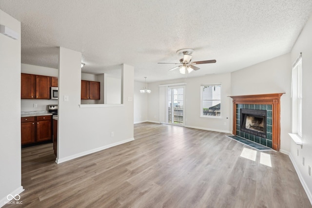 unfurnished living room featuring a textured ceiling, a tiled fireplace, ceiling fan with notable chandelier, and light wood-style floors