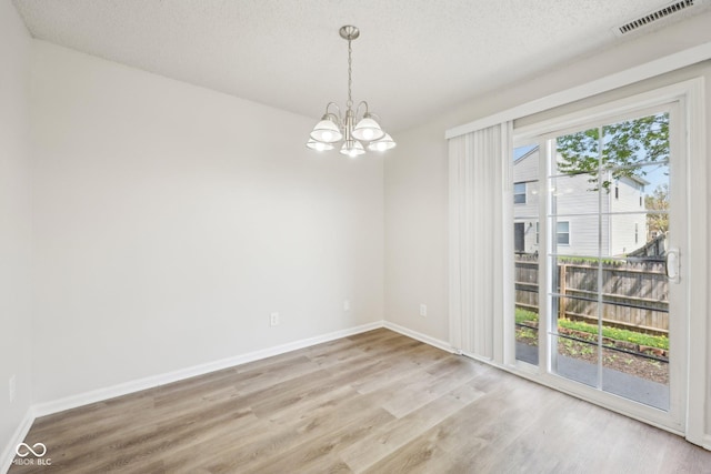 unfurnished room featuring an inviting chandelier, baseboards, wood finished floors, and visible vents