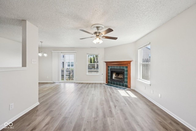unfurnished living room with a textured ceiling, ceiling fan with notable chandelier, wood finished floors, and a tile fireplace