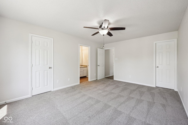 unfurnished bedroom with baseboards, ensuite bathroom, carpet, and a ceiling fan