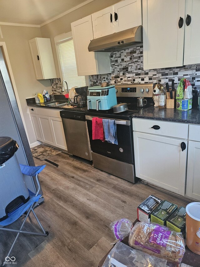 kitchen featuring appliances with stainless steel finishes, a sink, under cabinet range hood, ornamental molding, and dark wood-style floors