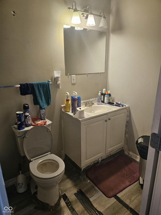 half bathroom featuring wood finished floors, toilet, vanity, and baseboards