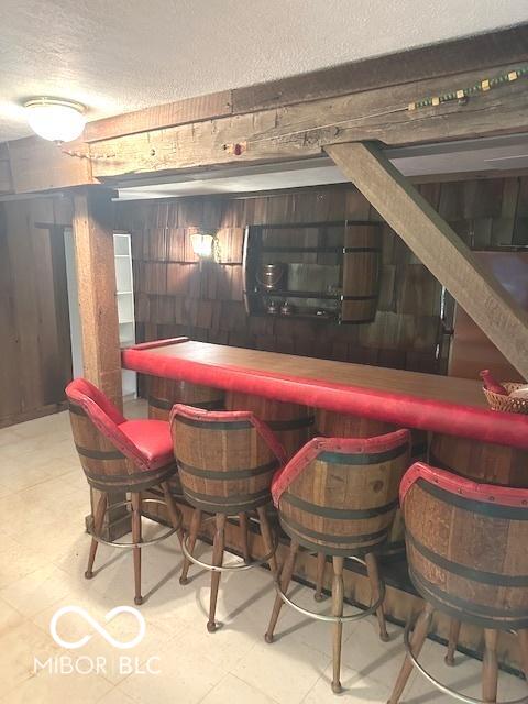 bar with a dry bar, a textured ceiling, tile patterned floors, and wooden walls