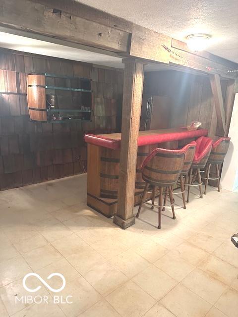 bar with a textured ceiling, wood walls, a bar, and tile patterned floors