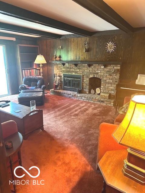 living room featuring carpet, a brick fireplace, beam ceiling, and wooden walls