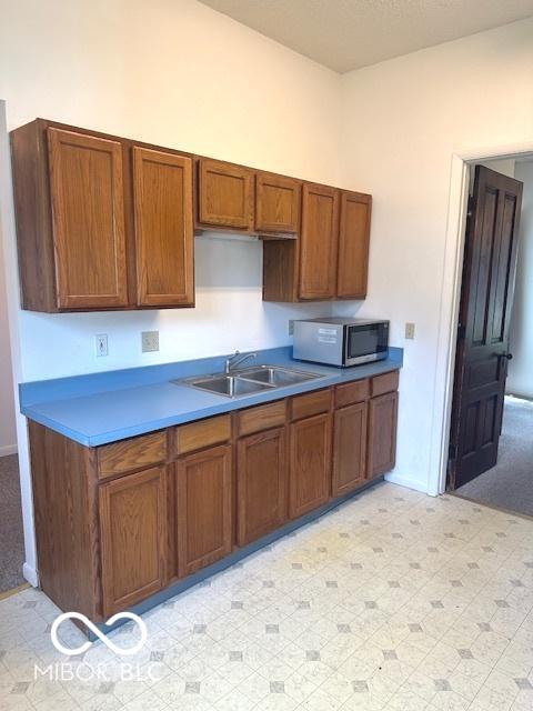 kitchen featuring stainless steel microwave, baseboards, brown cabinets, and a sink